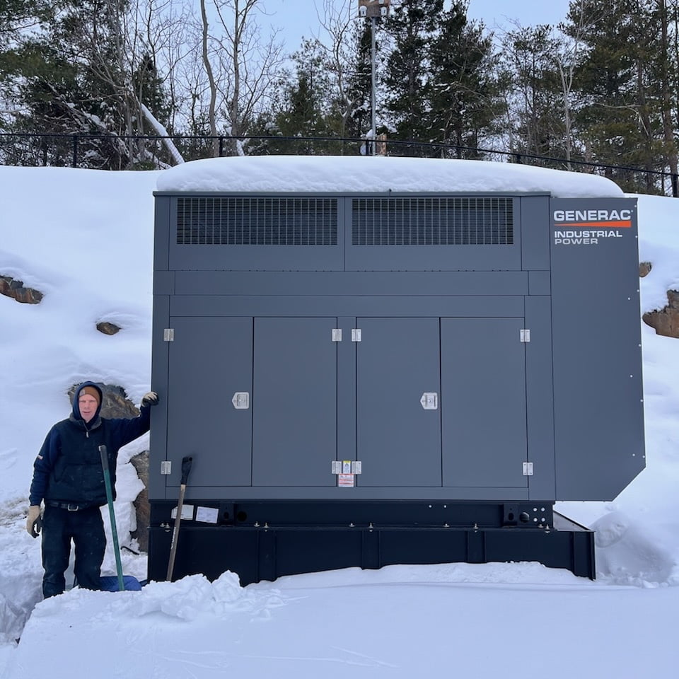 Backup generator installation in snowy rural Nova Scotia with technician beside a Generac Industrial Power system.